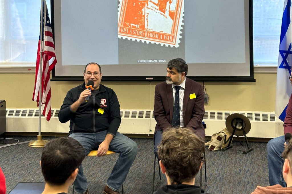 two men sitting in front of teens giving a talk.